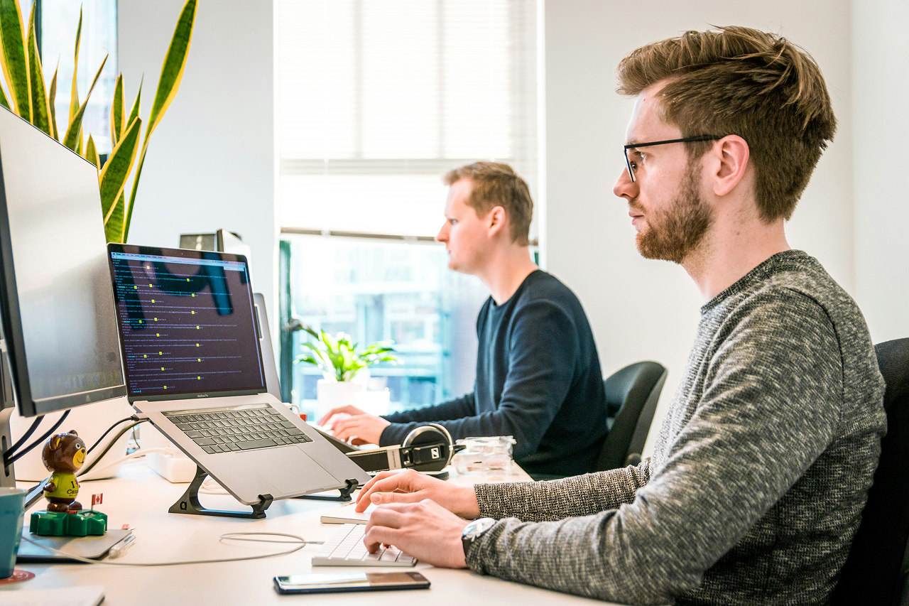 Two men sitting in the front of their computers, working.